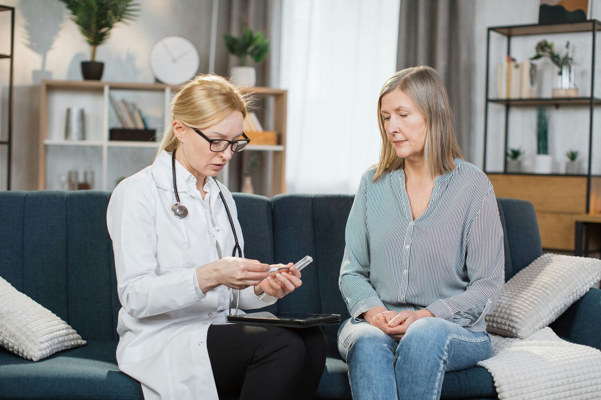 Doctor discussing notes with a seated patient on a couch in a bright living room