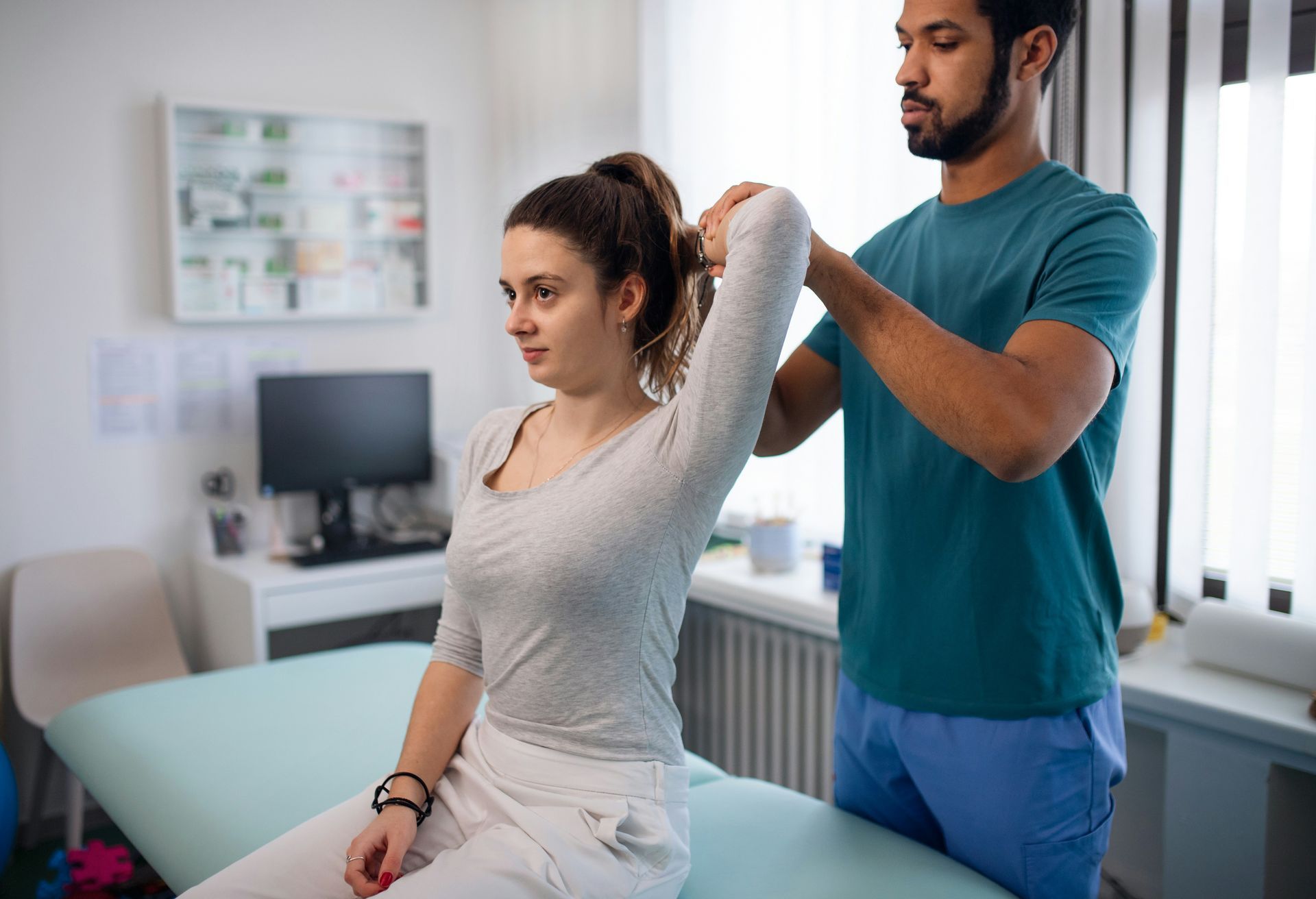 Physical therapist assisting a patient with an arm stretch in a clinic exam room