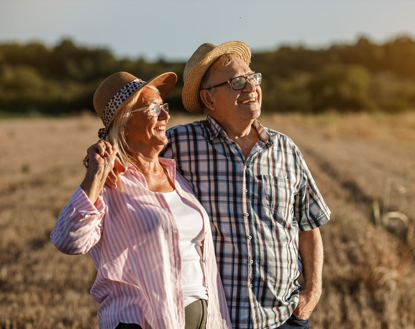 Two people in sun hats stand in a field, smiling and looking into the distance.