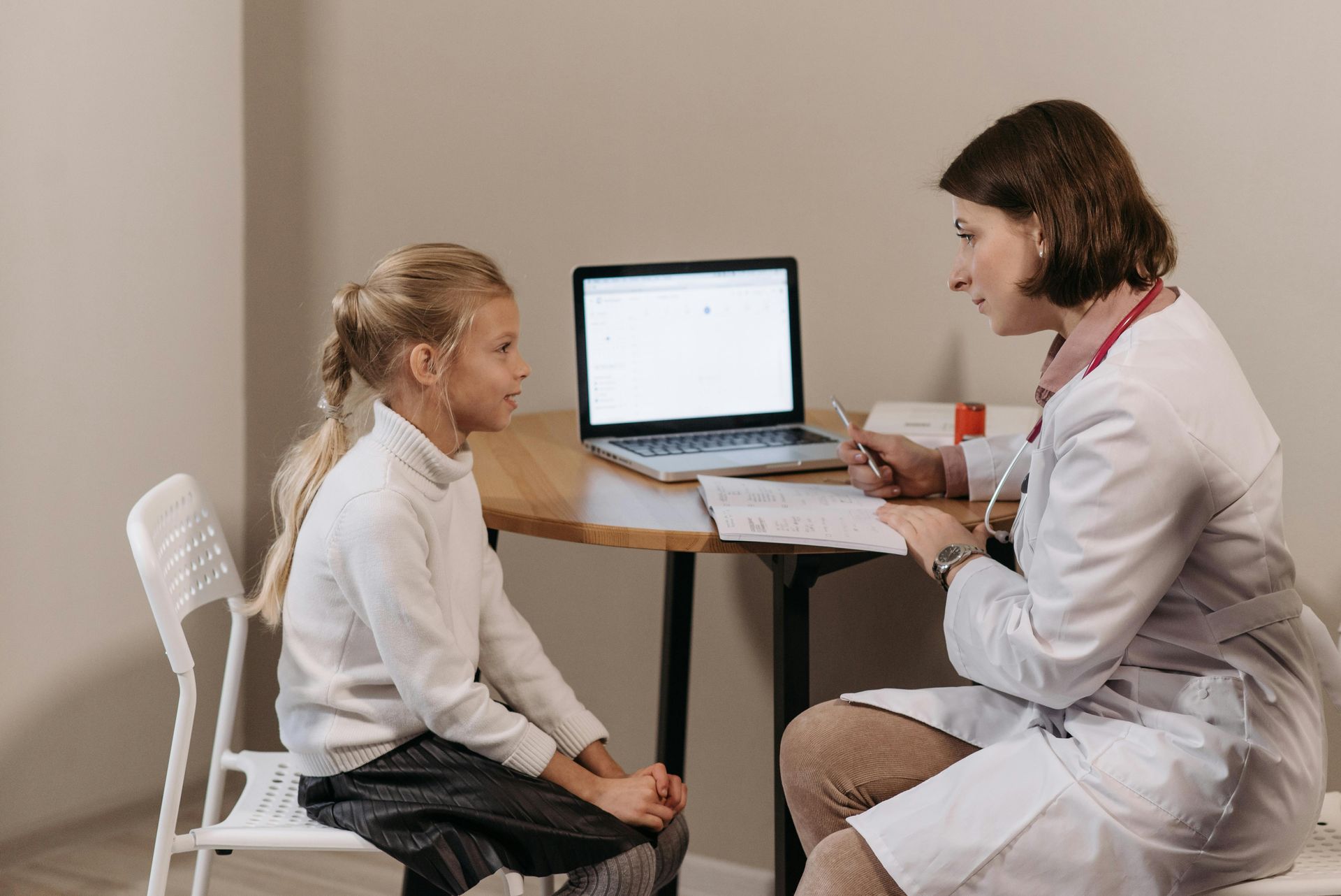 Doctor speaking with a child patient beside a laptop in a clinic room