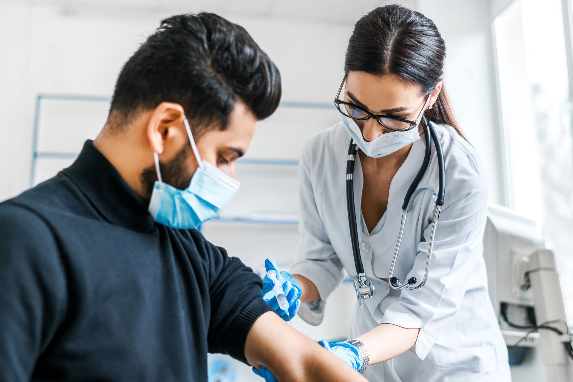 Healthcare worker taking blood pressure of a masked patient in a clinic