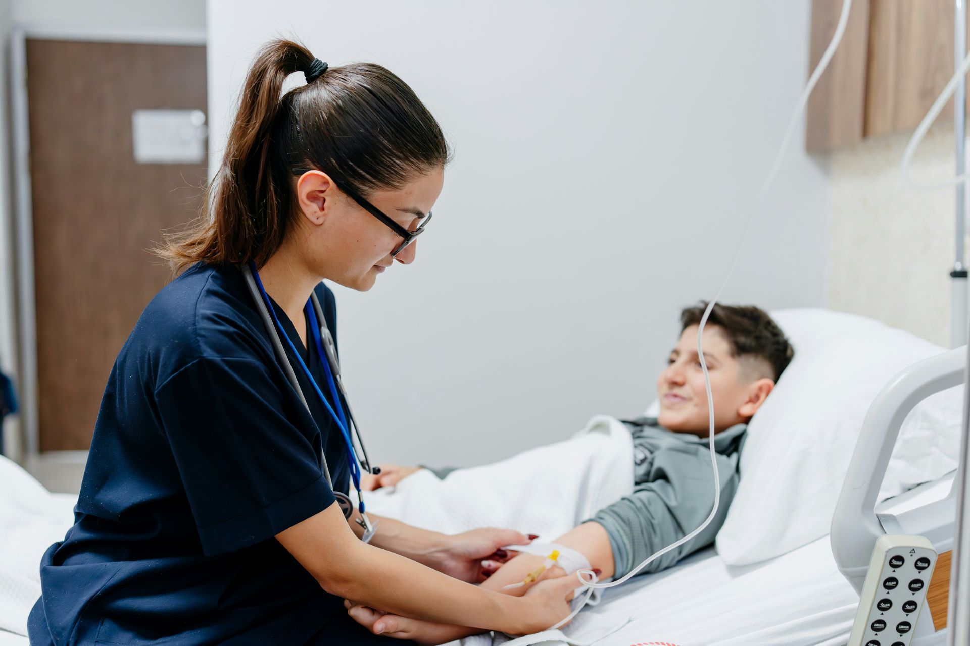 Nurse checking a patient’s arm IV while he lies in a hospital bed