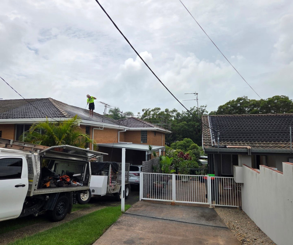 Residential driveway with white gate, parked vans, and a worker on a roof under an overcast sky