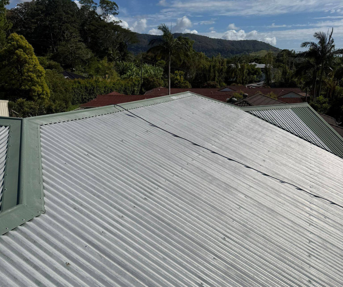 Corrugated metal roof in the foreground with green trees and distant hills under a cloudy sky