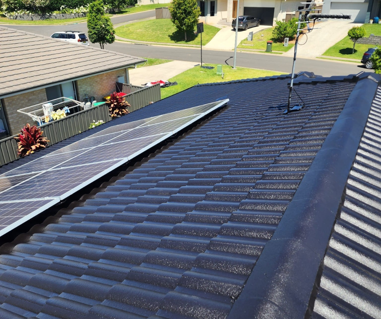 Solar panels on a dark tiled roof in a suburban neighborhood.