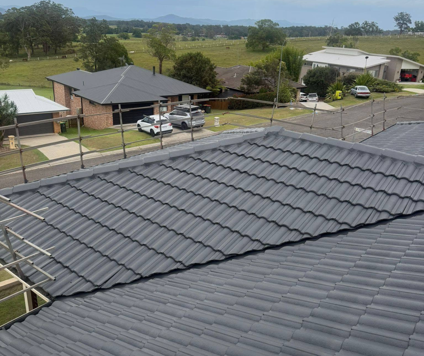 Grey tiled rooftops in a suburban neighborhood under a clear sky, with trees and houses in the background