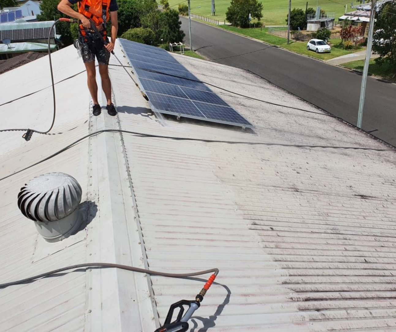 Worker inspecting solar panels on a rooftop next to a vent and ladder in bright daylight