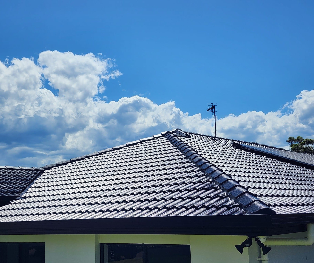 Blue tiled house roof under a bright sky with clouds