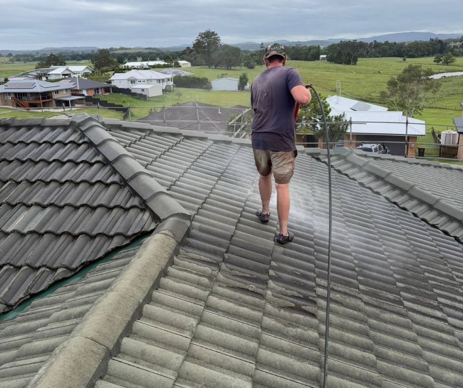 Person walking on a gray tiled roof in a suburban area with green fields in the background