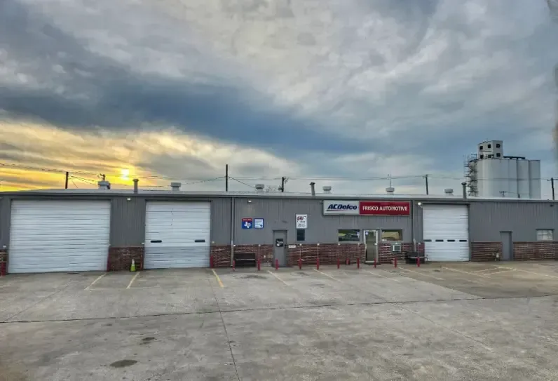 Industrial building with garage doors, red carts, and a cloudy sky at sunset | Frisco Automotive & Transmission