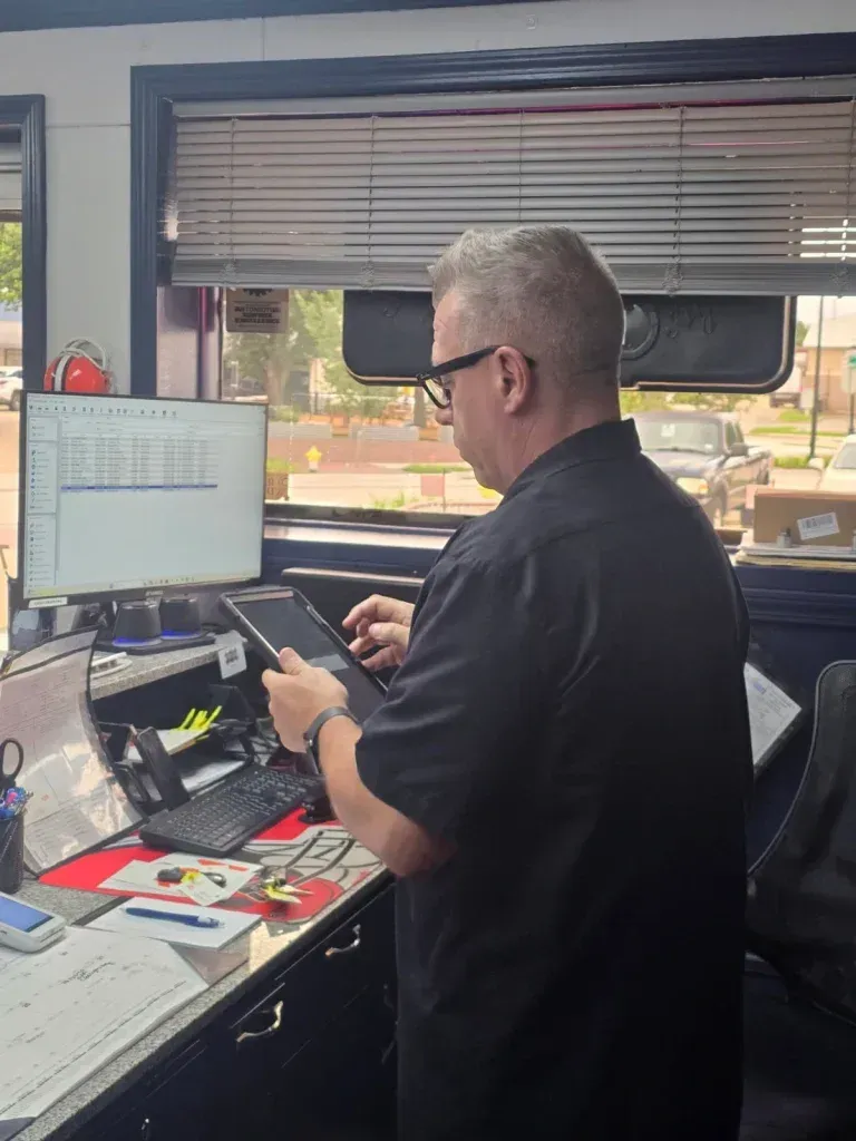 Person working at a desk with dual monitors and a phone in an office or control room. | Frisco Automotive & Transmission