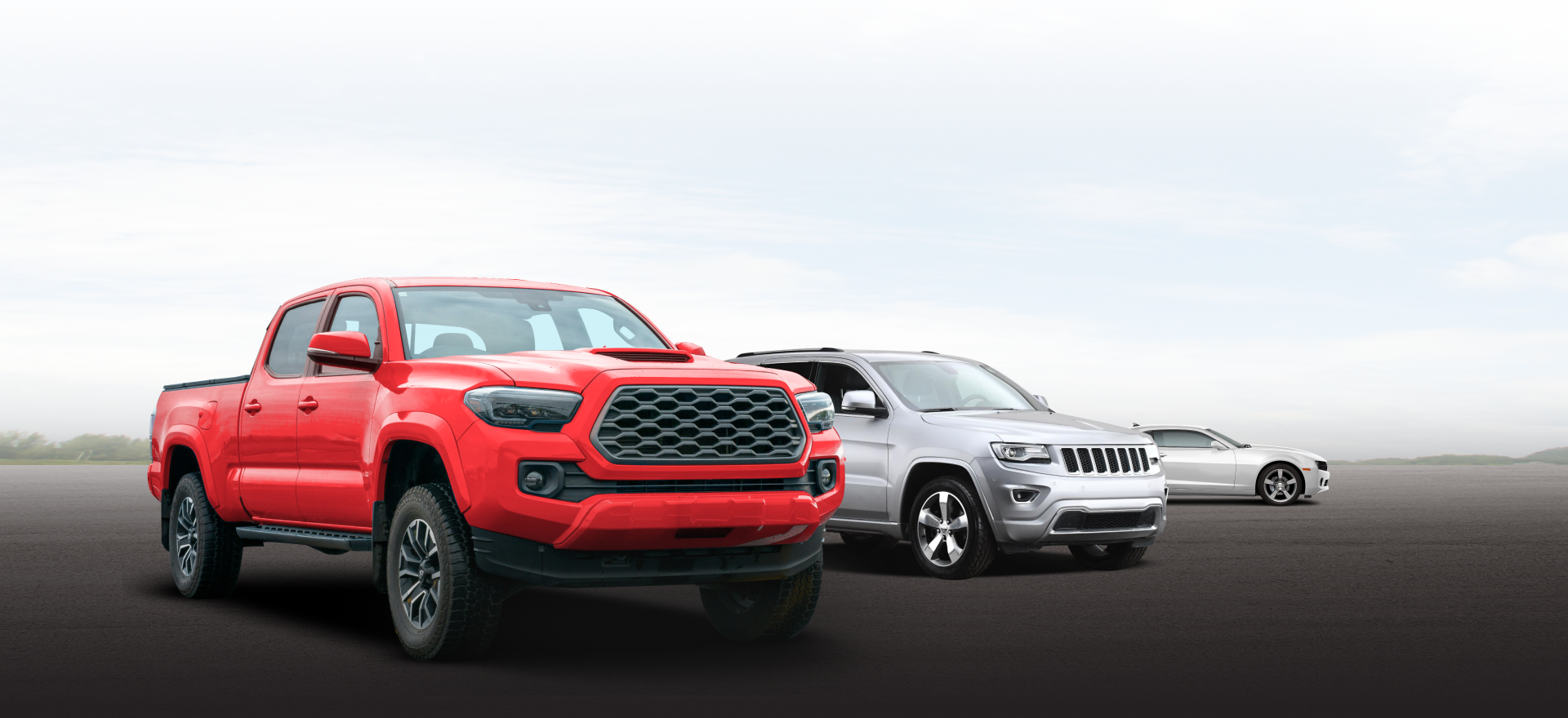Red, silver, and gray pickup trucks lined up on a road under a bright sky. | Frisco Automotive & Transmission