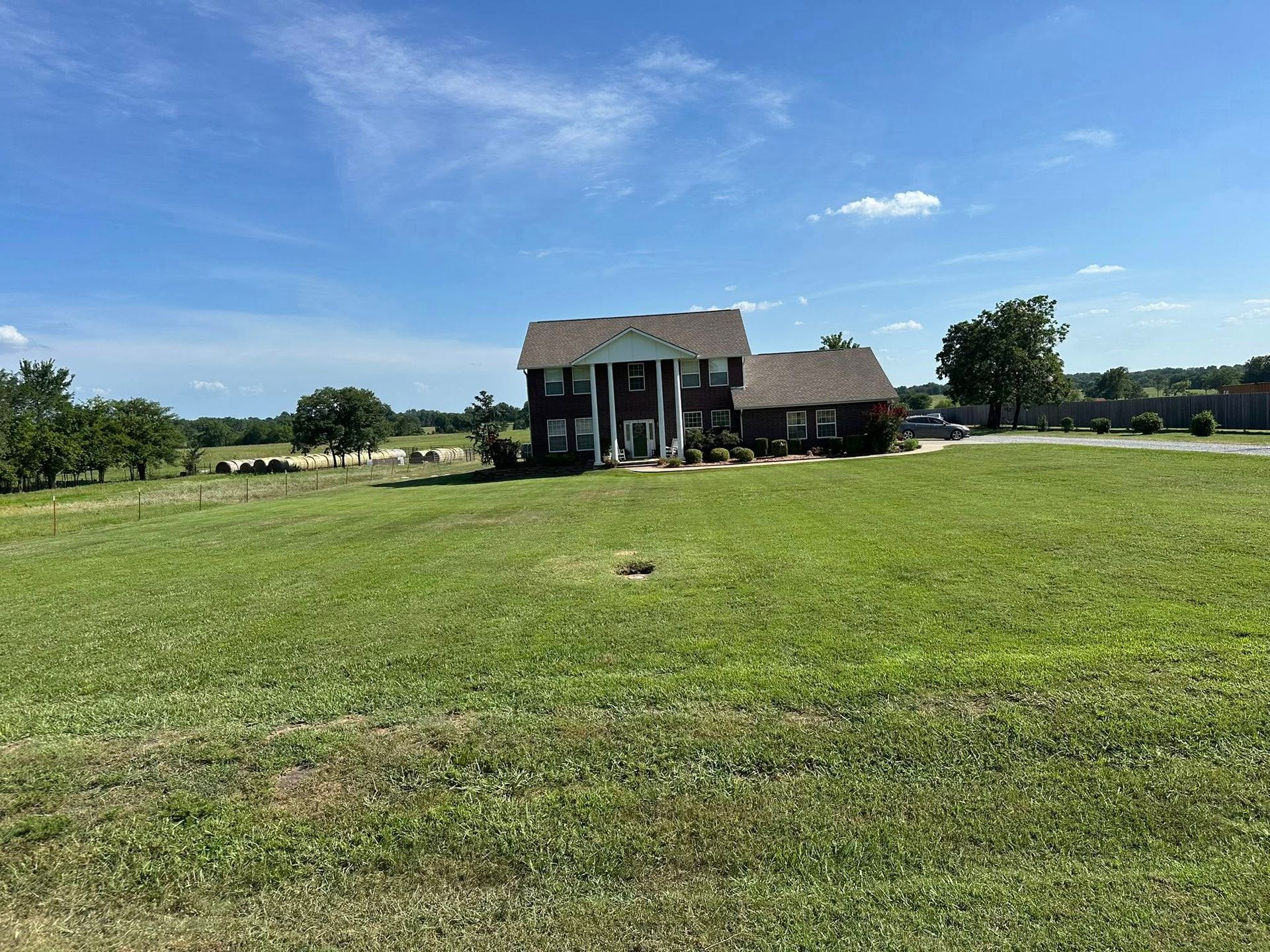 Large house with white columns, on a grassy hill under a blue sky with scattered clouds.