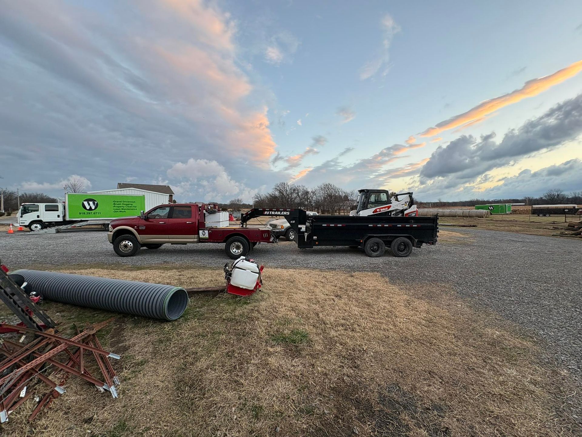 Red pickup truck towing a black trailer with a small excavator, under a cloudy sky.