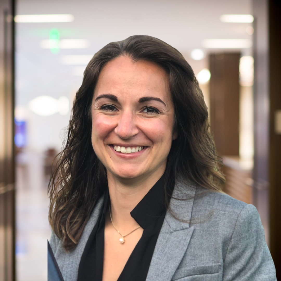 A woman in a grey jacket and black shirt is smiling for the camera.