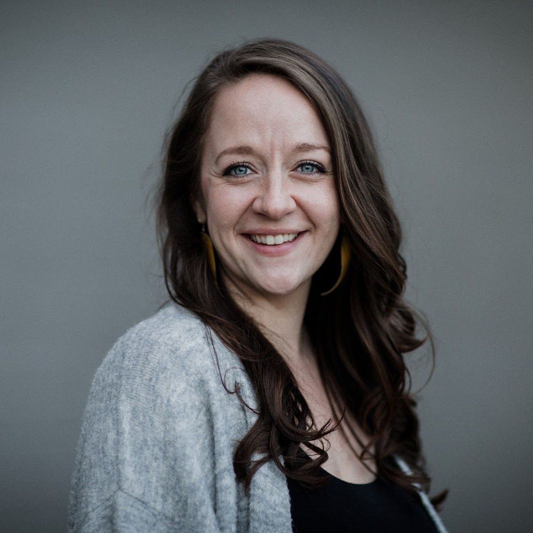 A woman wearing a gray sweater and a black shirt is smiling for the camera.