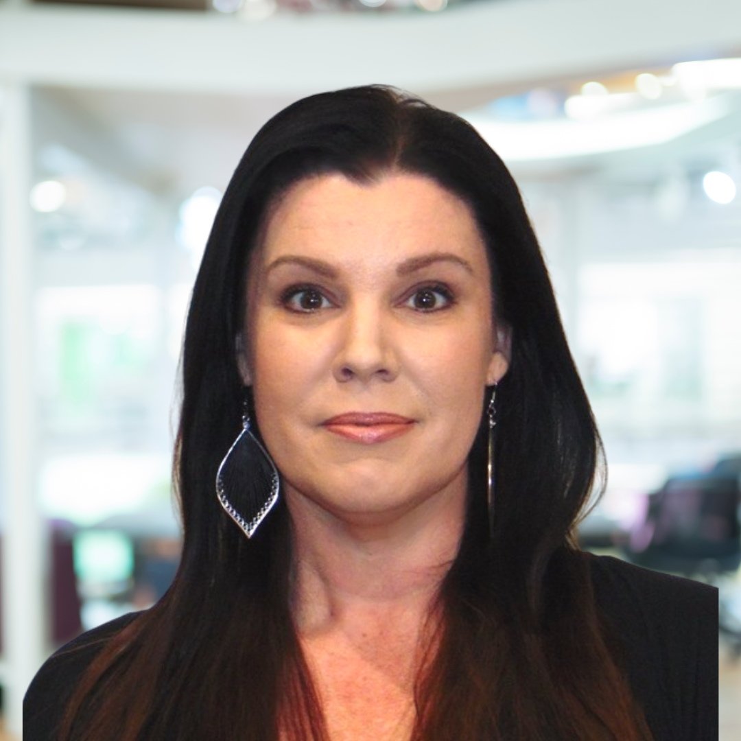 A woman wearing earrings and a black jacket looks at the camera