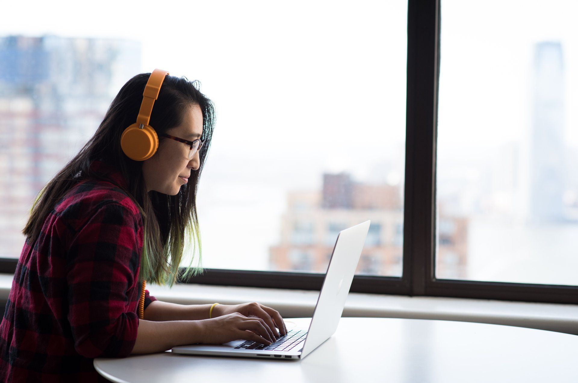 A woman wearing headphones is typing on a laptop computer.