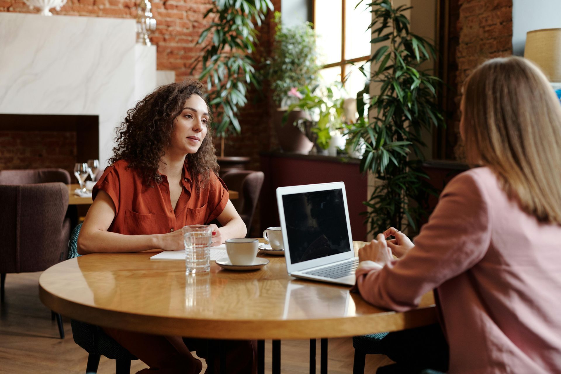 Two Ladies sitting around a table for an interview with an open laptop on the table, a glass of water and two tea cups