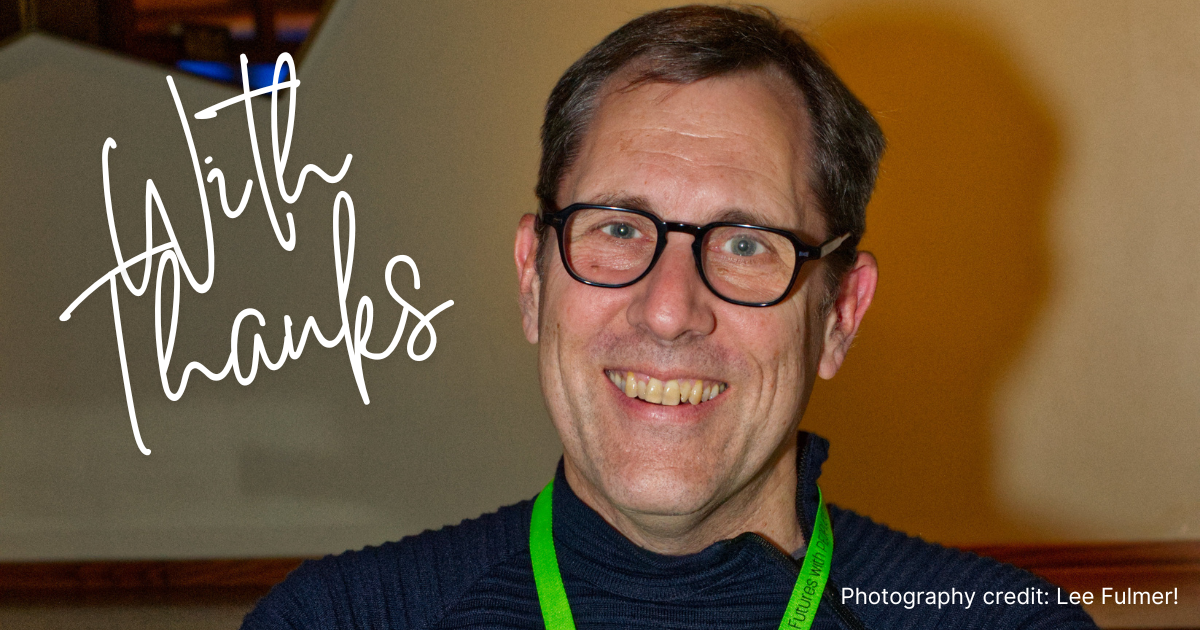 Smiling man with glasses and green lanyard beside handwritten “with thanks” text