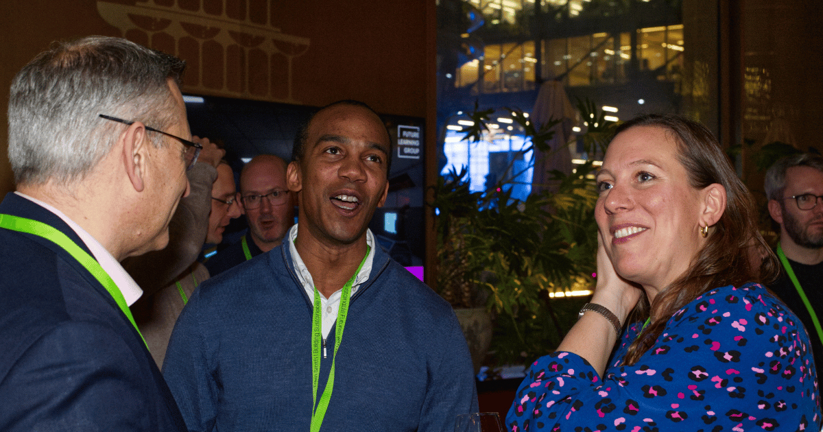 Three people talking at a nighttime event, wearing green lanyards and smiling.