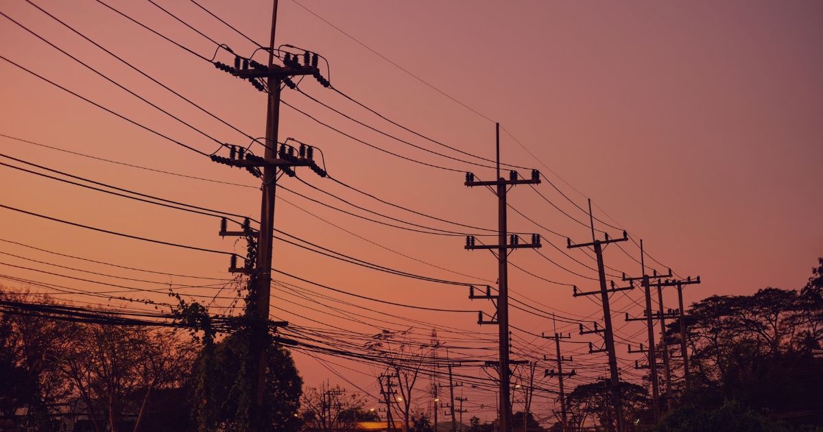 Utility poles and power lines silhouetted against a pink-orange sunset sky.