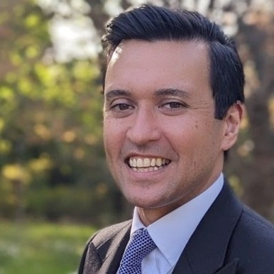 Smiling man in a suit outdoors with blurred trees in the background