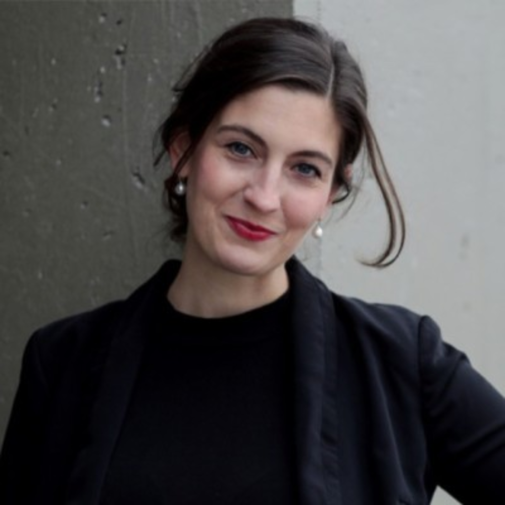 Portrait of a smiling woman in a black top and jacket against a gray wall