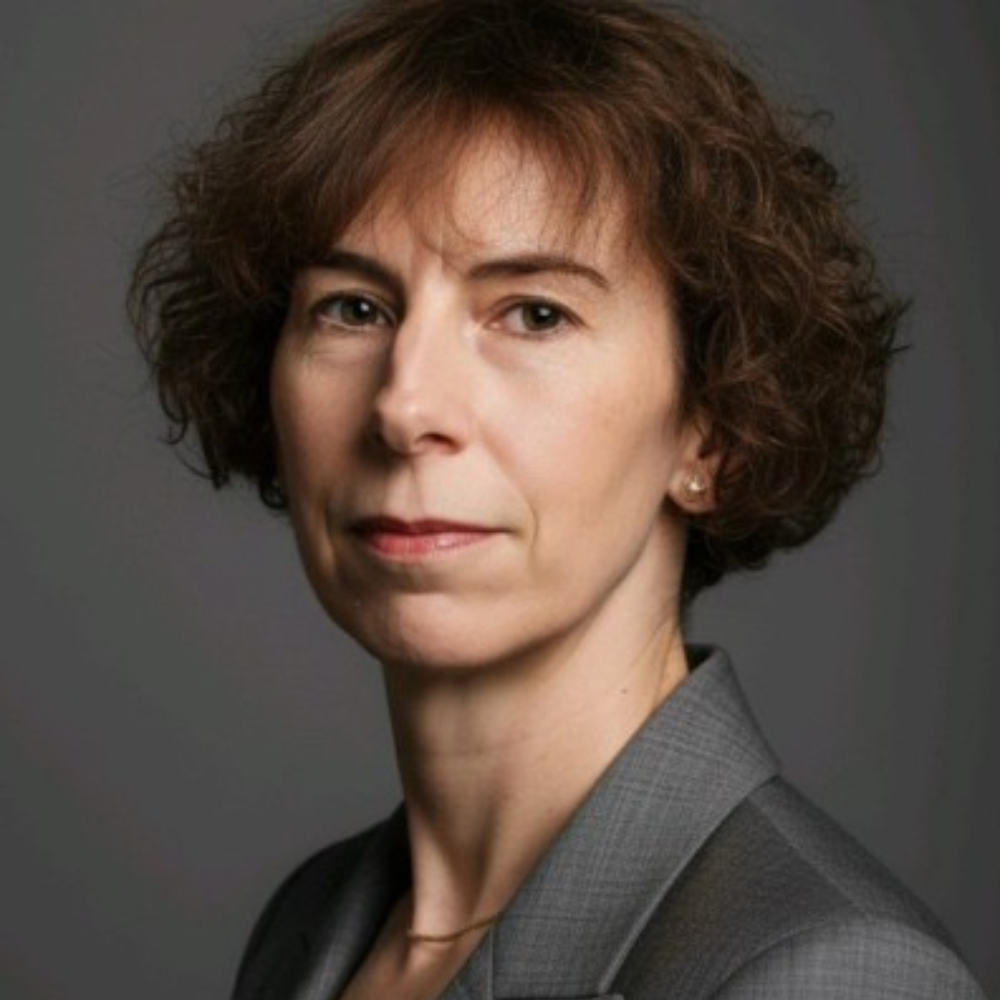 Studio portrait of a woman in a gray blazer, looking at the camera with a neutral expression