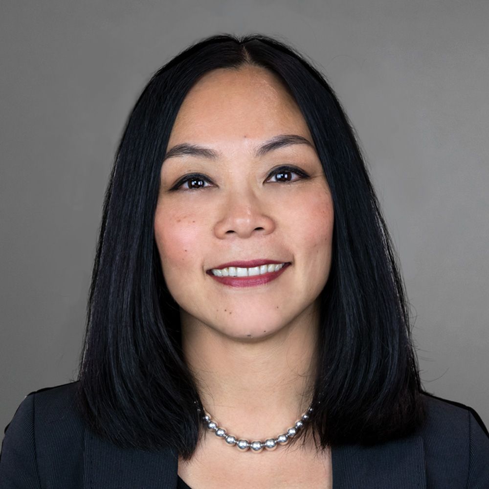 Portrait of a smiling person with straight black hair against a gray background