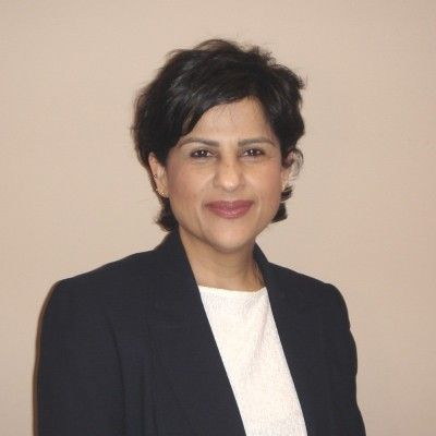 Portrait of a smiling person in a dark blazer and white top against a beige background
