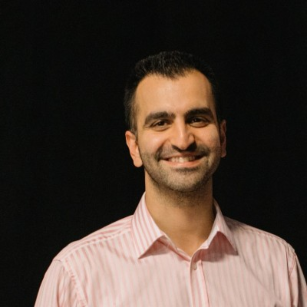 Smiling man in a pink striped shirt against a dark background