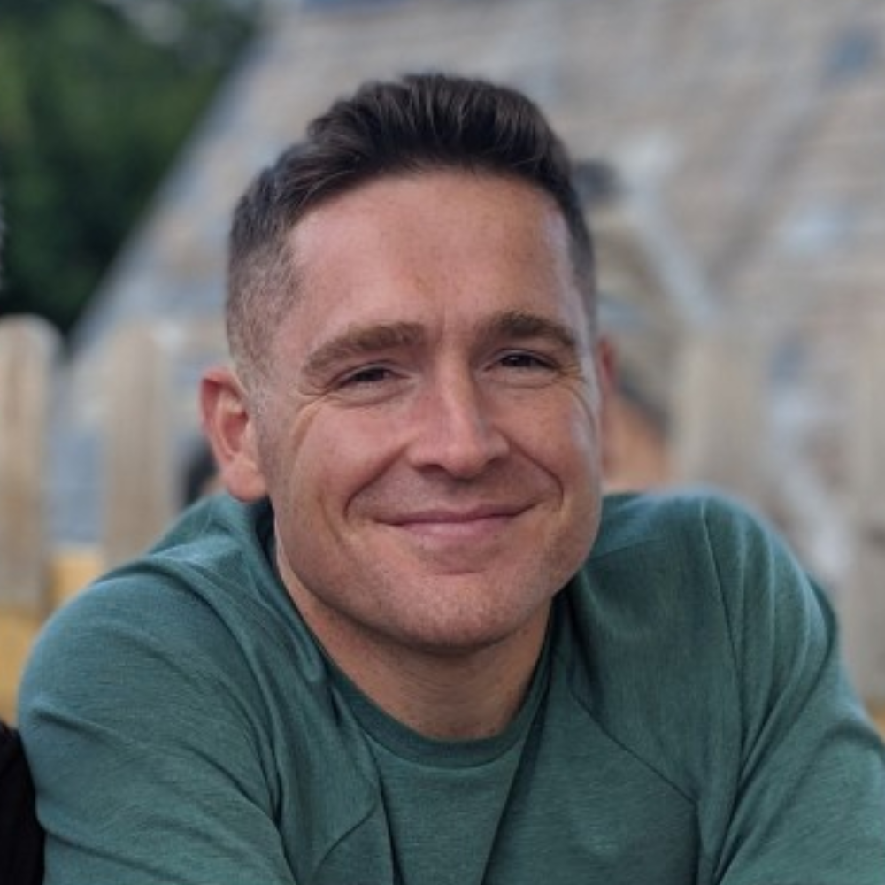 Smiling man in a green shirt outdoors with a blurred stone background