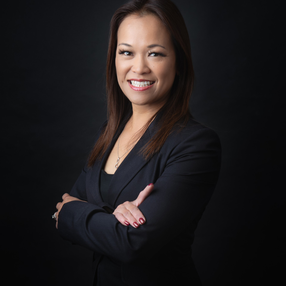 Smiling person in a black blazer with arms crossed against a dark background