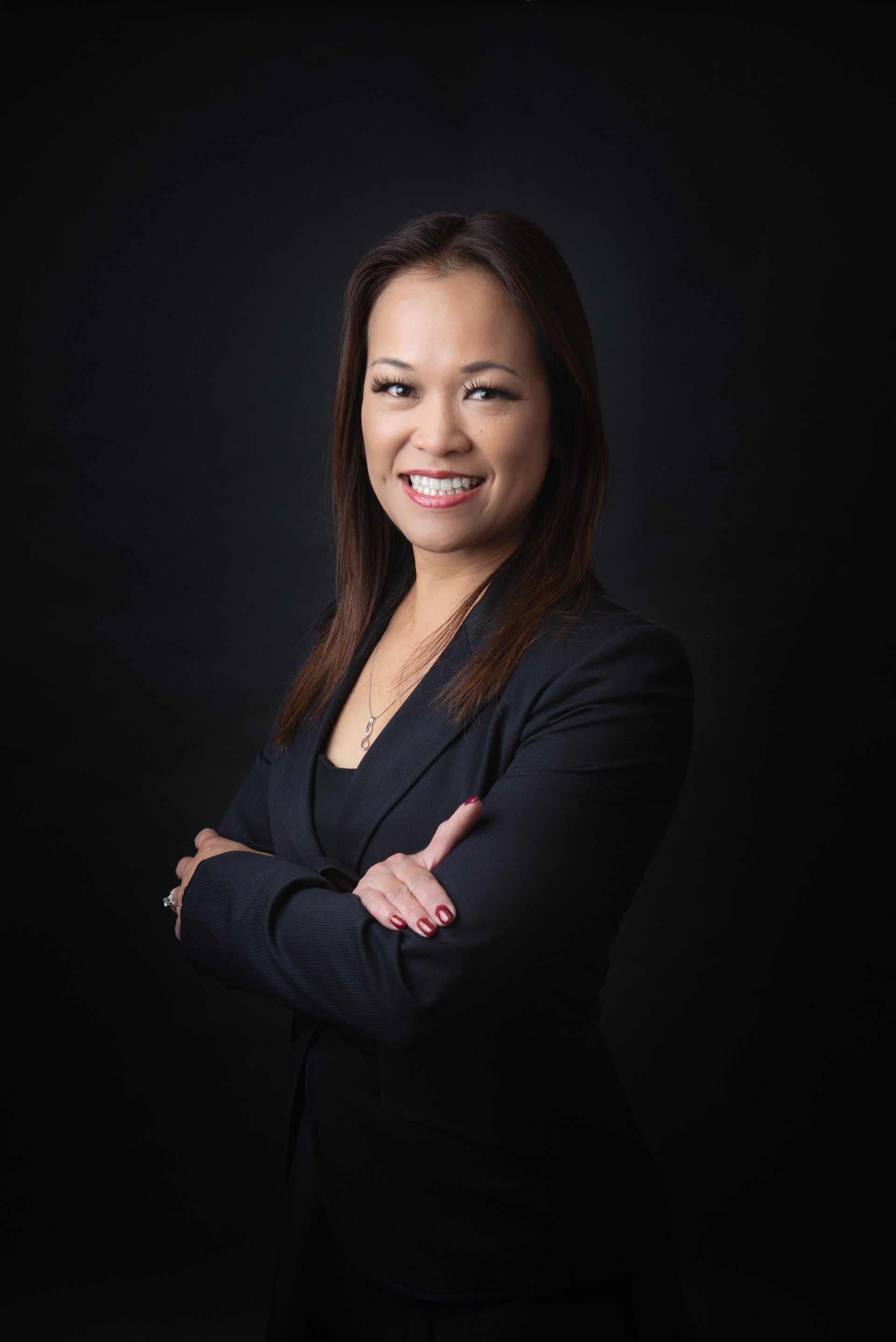 Smiling professional in a black blazer with arms crossed against a dark background
