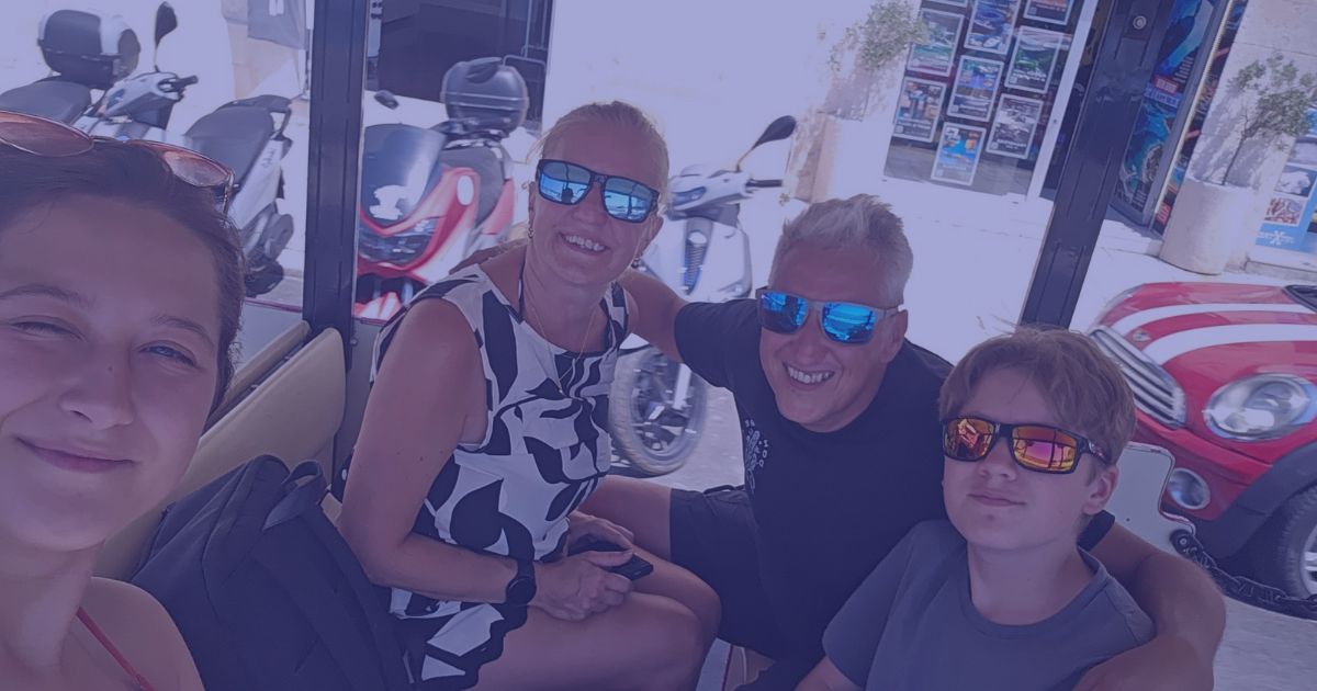 Five people wearing sunglasses pose for a selfie on a sunny outdoor terrace.