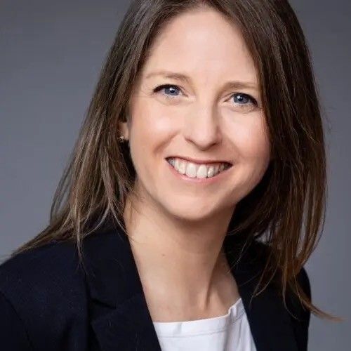 Smiling woman in a dark blazer and white top against a gray background
