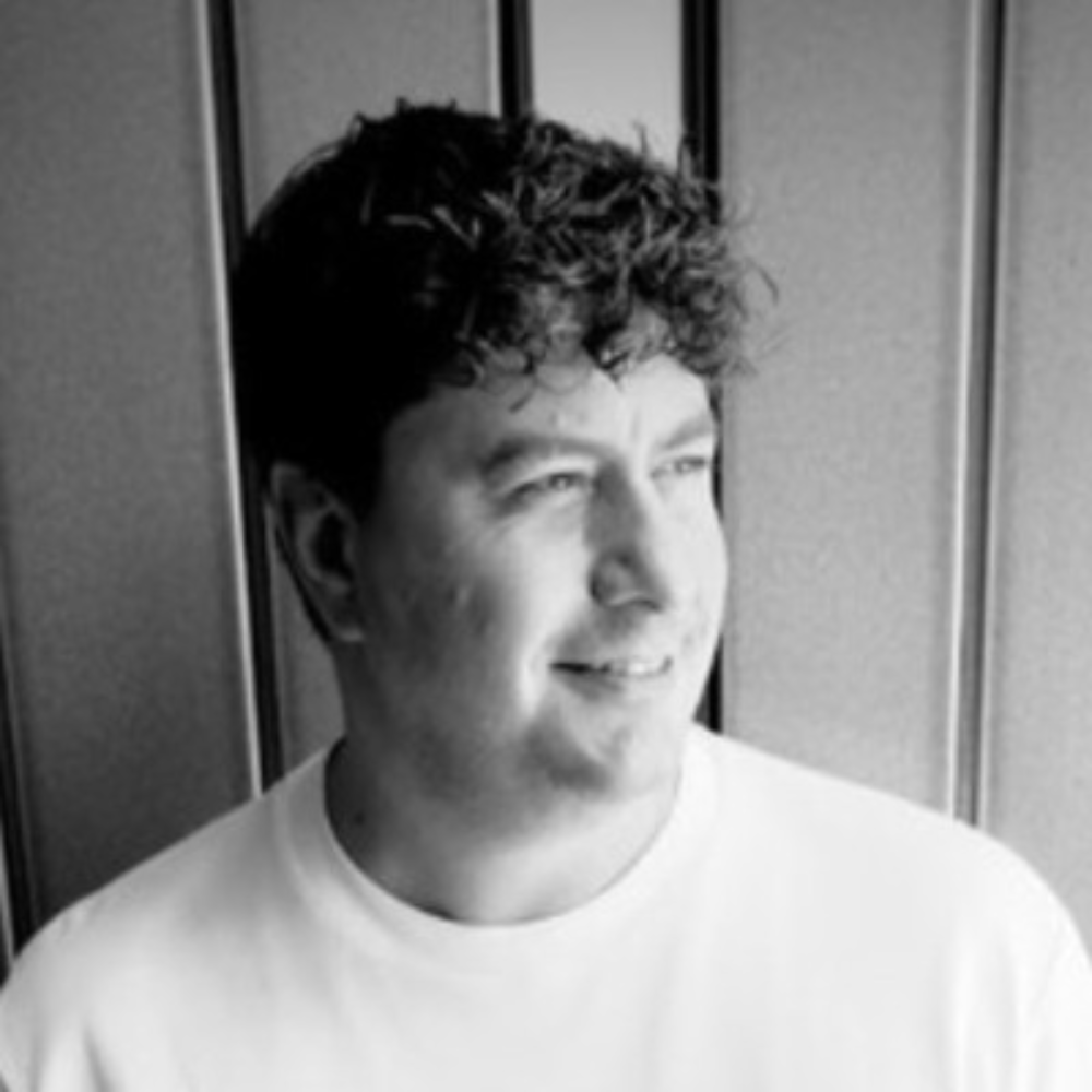 Person in a white T-shirt looking to the side, against a paneled wall.