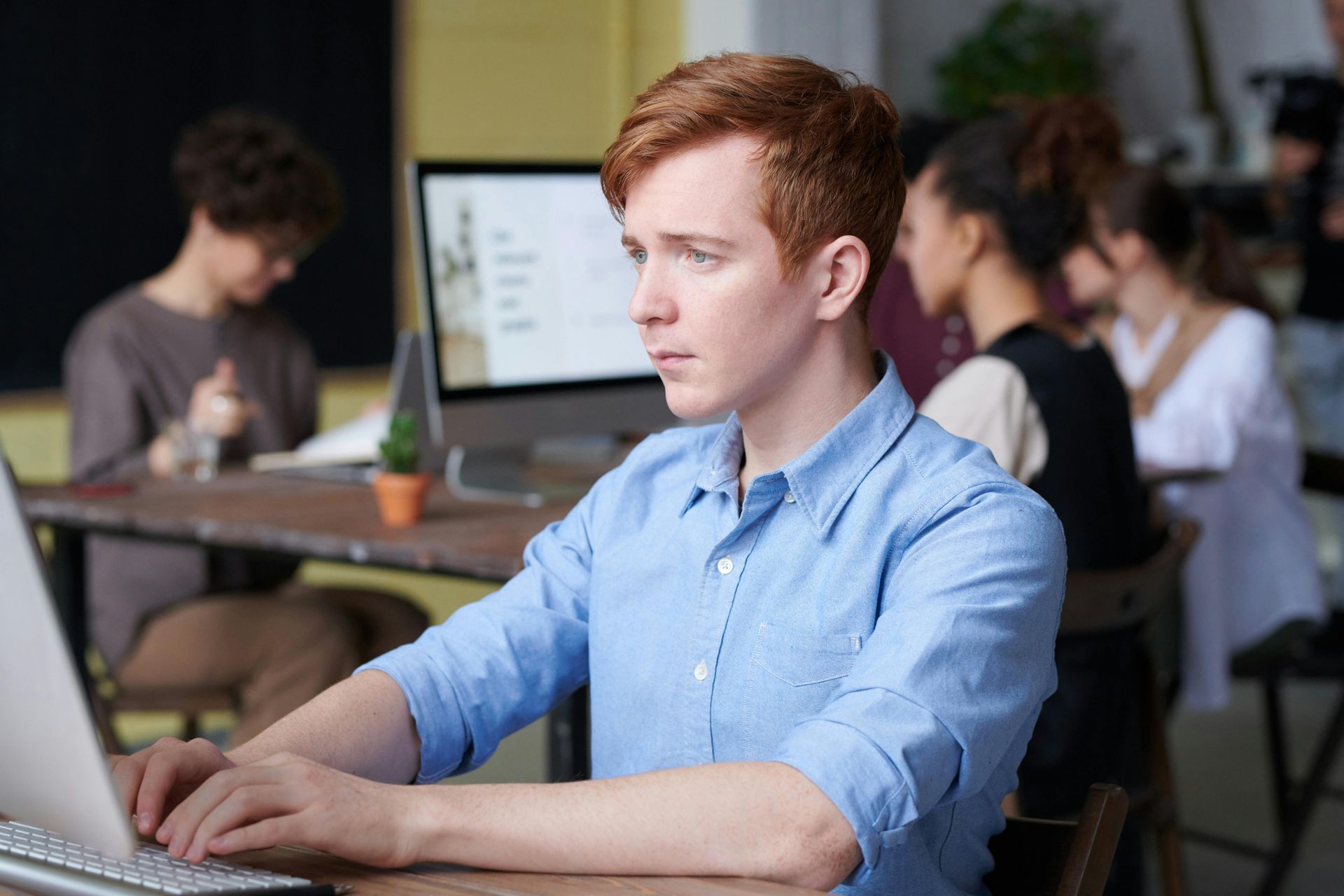 Person in a blue shirt working on a laptop in a busy office setting