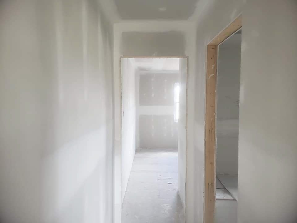 Picture looking down a freshly drywalled hallway. Mudding and taping are complete