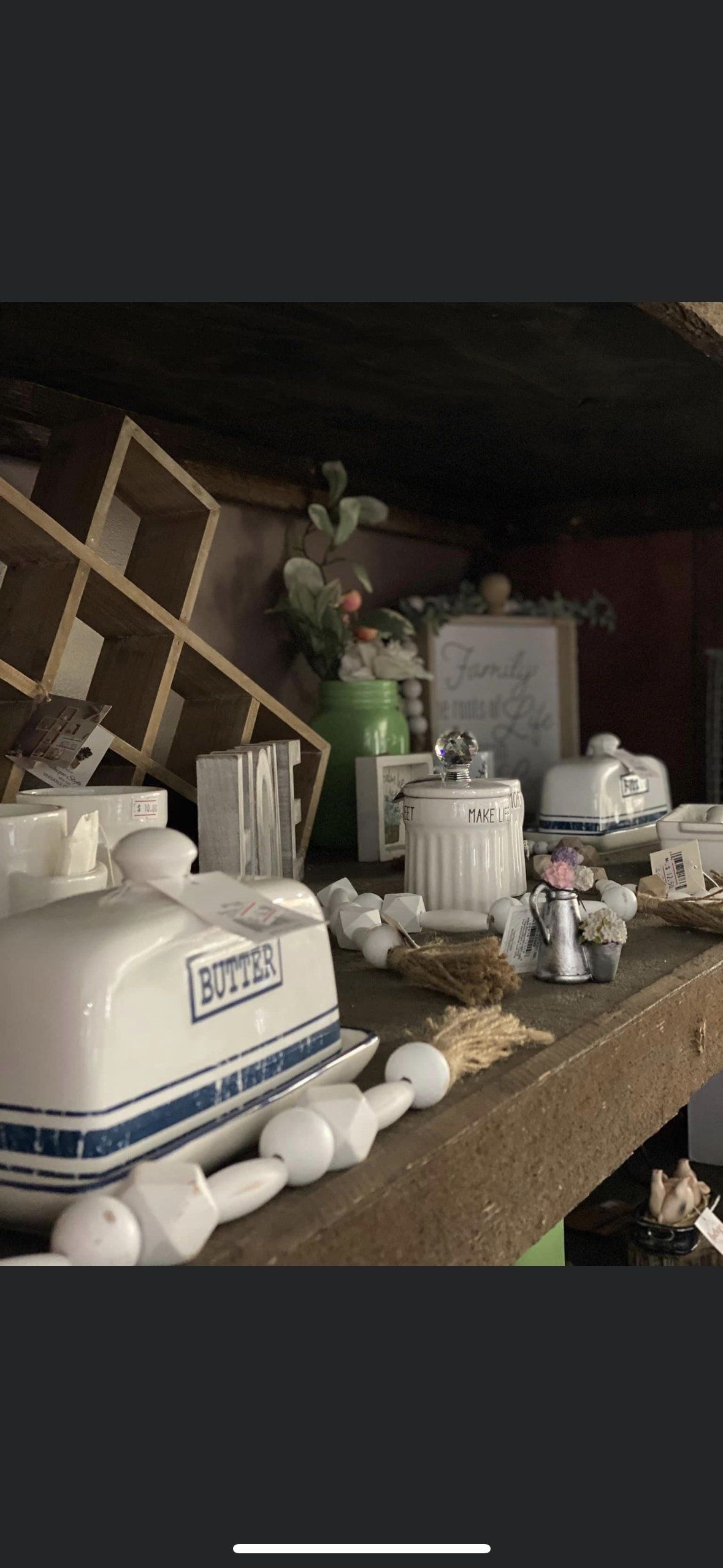 A wooden shelf displays white ceramic kitchen decor, including butter dishes and a wooden lattice frame, in a rustic style.