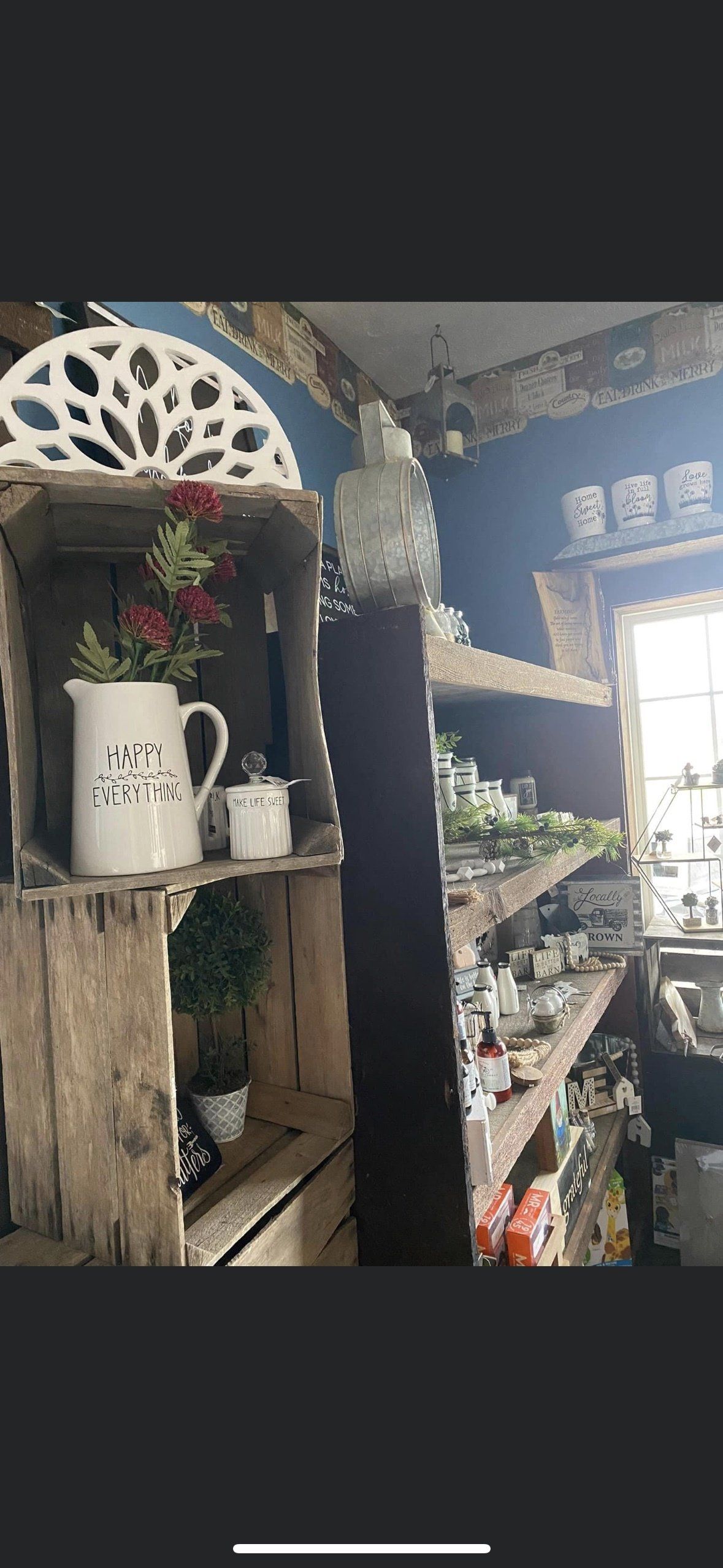 Rustic wooden crates stacked on shelves hold a white pitcher with red flowers, glass decor, and various small trinkets.