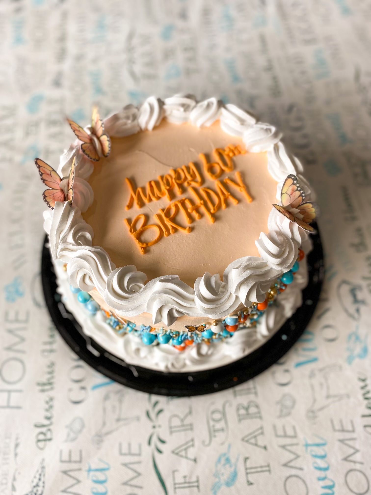 A birthday cake with peach frosting, white piping, butterflies, and colorful sprinkles, labeled