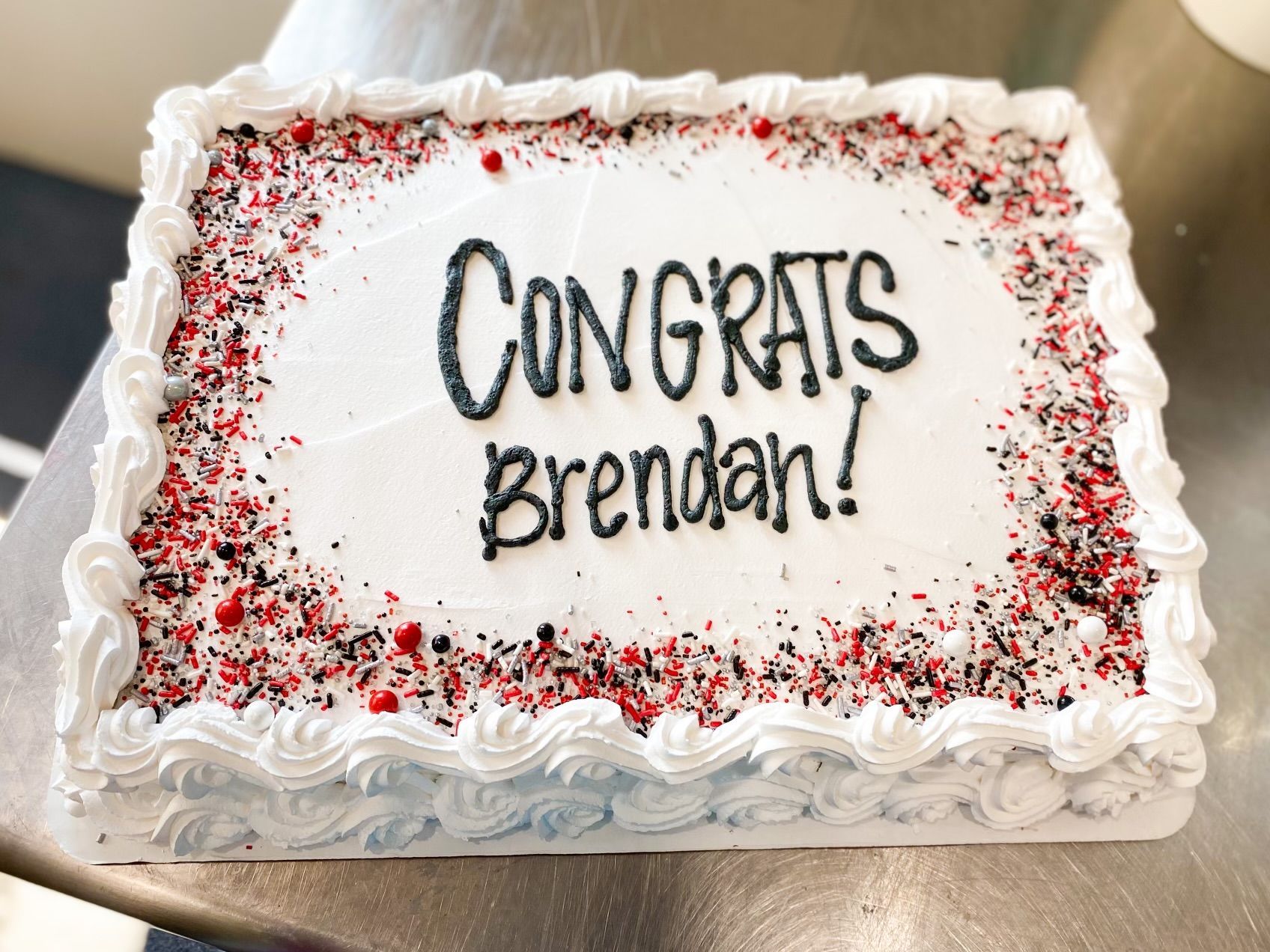 A rectangular sheet cake with white frosting, black text reading