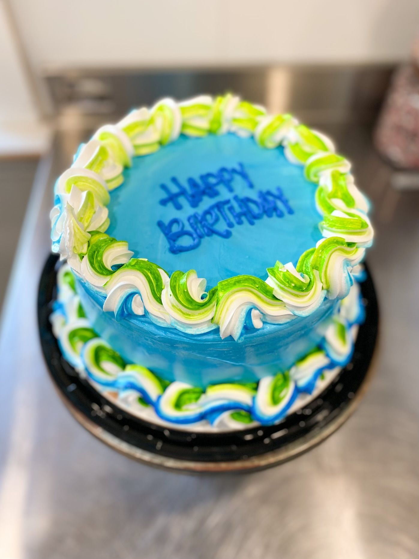 A round blue birthday cake with lime green and white piped frosting borders and
