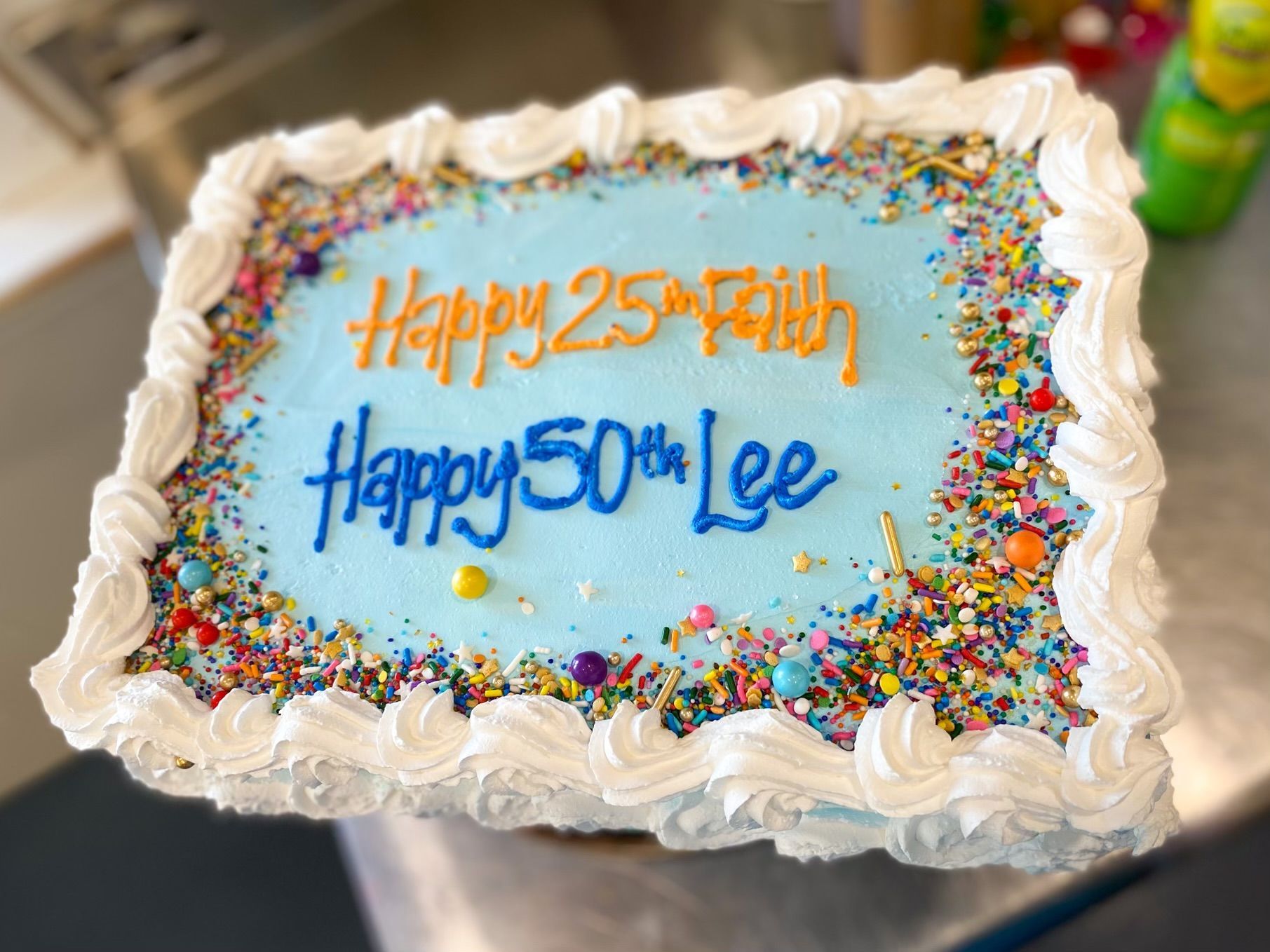 A rectangular cake with blue frosting, white borders, and sprinkles, inscribed