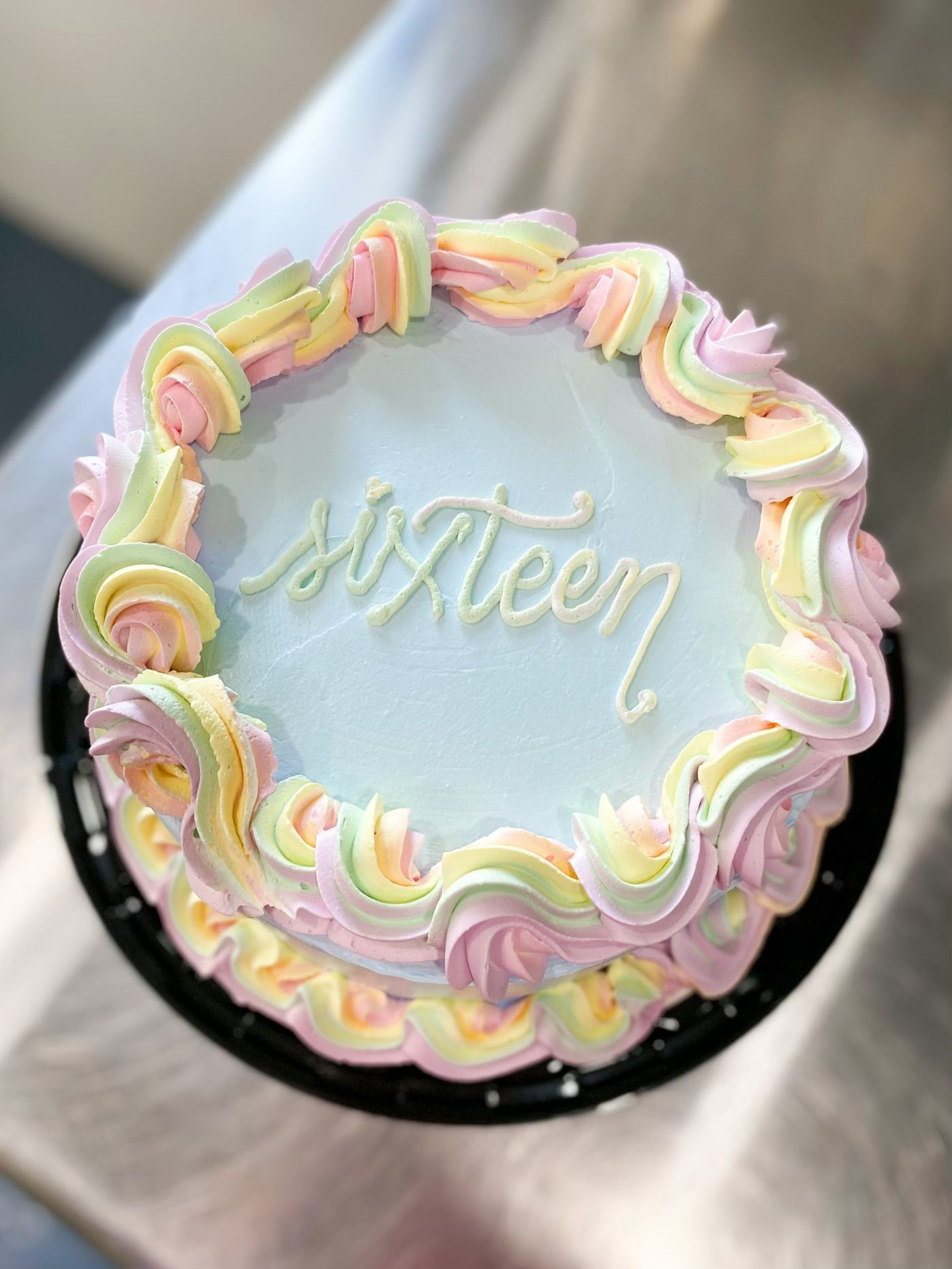 A light blue cake with pastel pink, yellow, and green piped frosting swirls, with