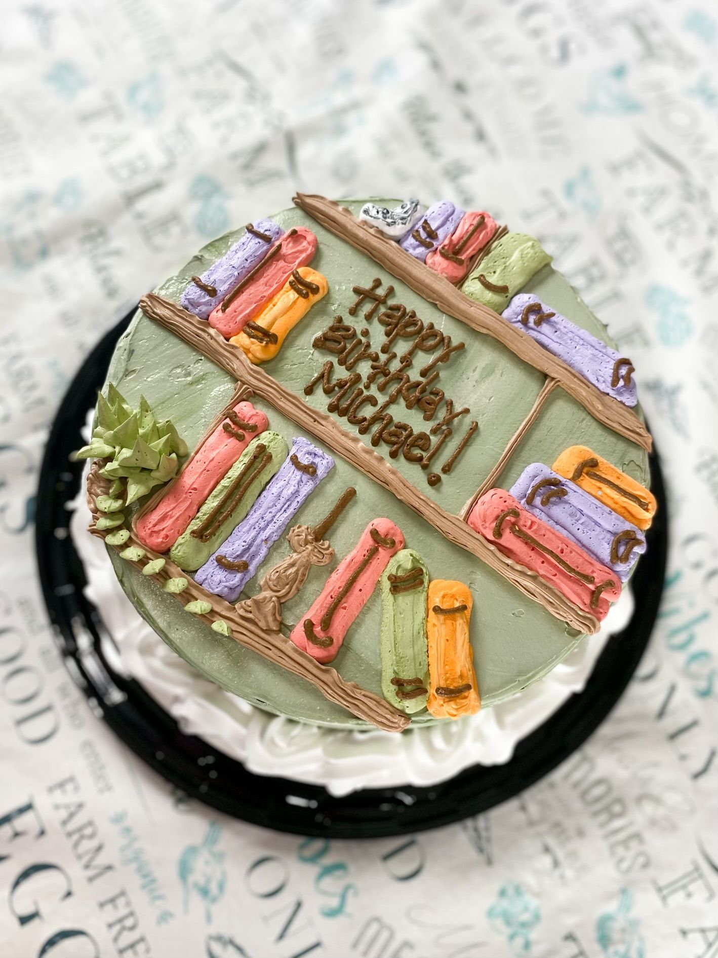 A round birthday cake with sage green frosting, decorated with piped icing