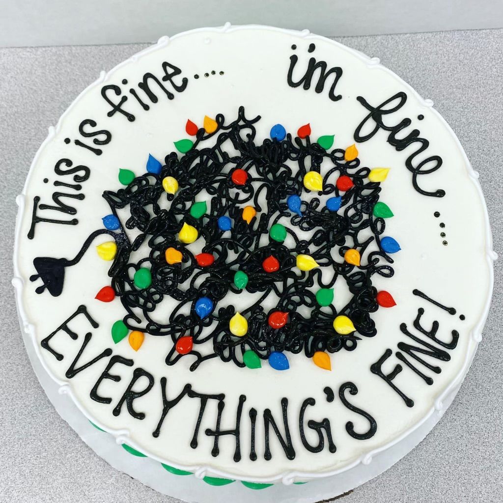 A white round cake decorated with a tangled, black-piped ball of Christmas lights and the text