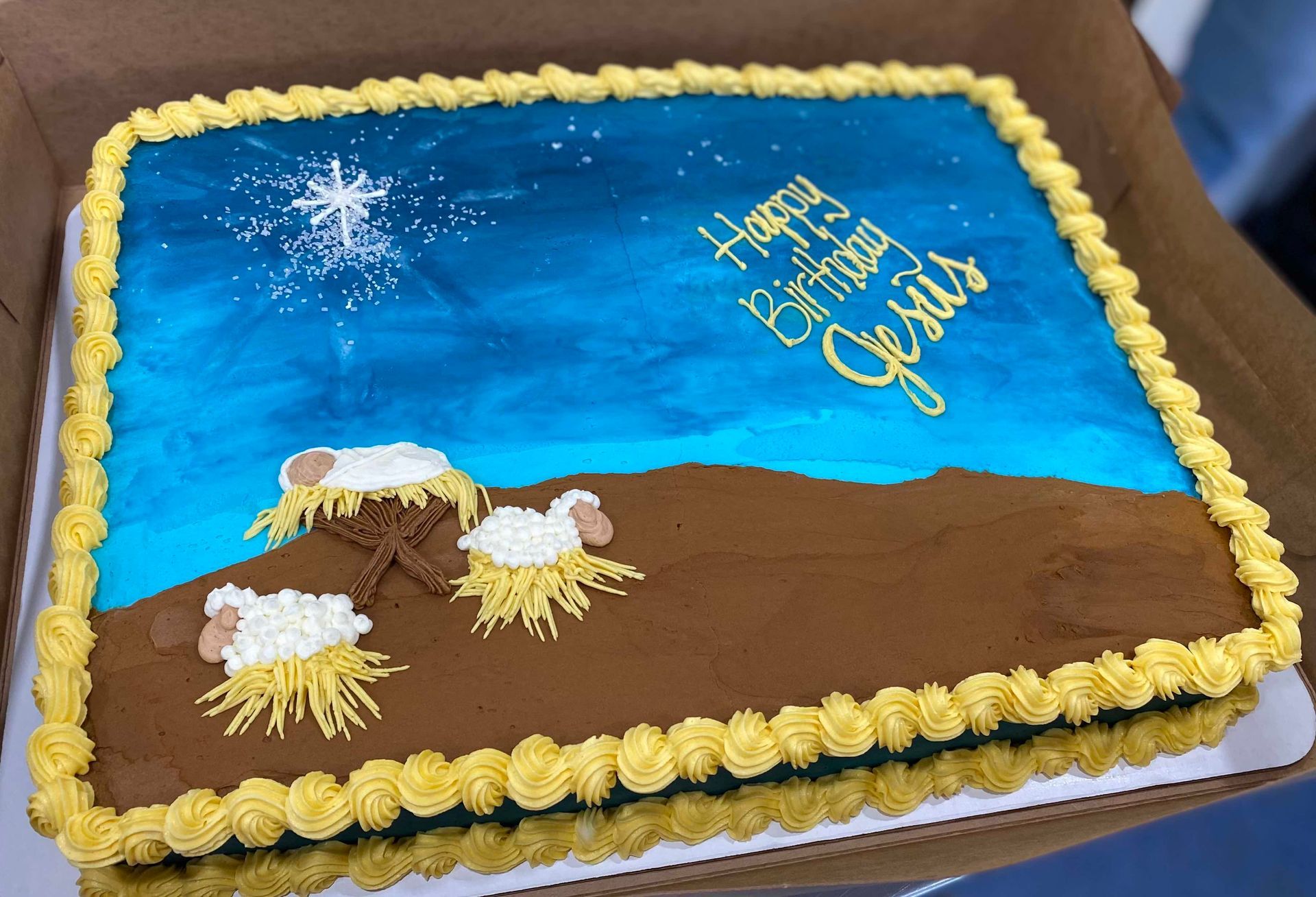 A rectangular sheet cake with a blue night sky, a star, and two sheep over brown ground, inscribed